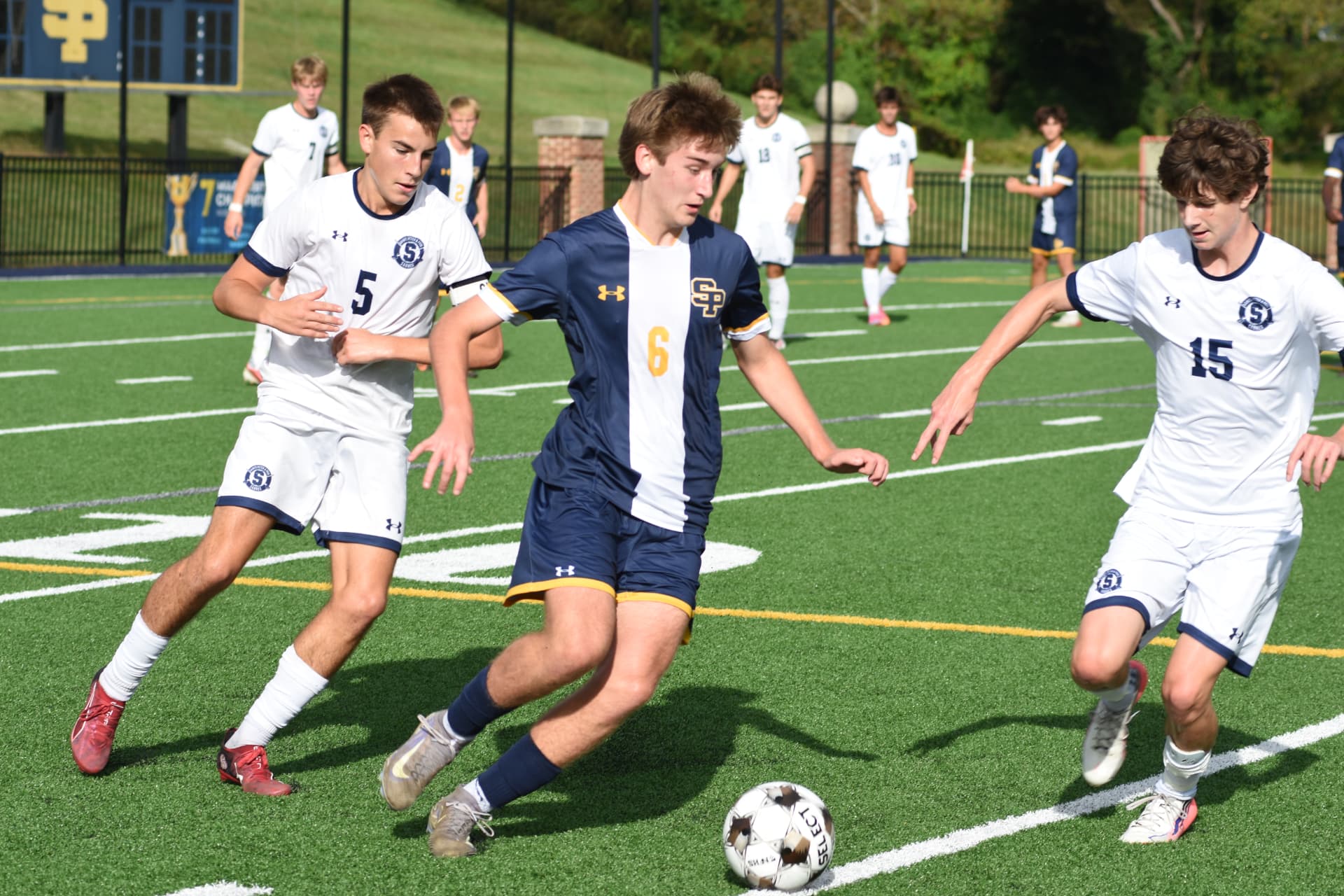 St. Paul's number 6 dribbles between two StP&P defenders